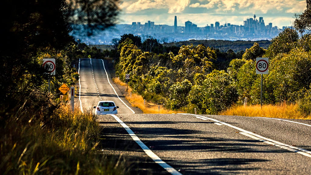Car driving along an empty country road towards a city