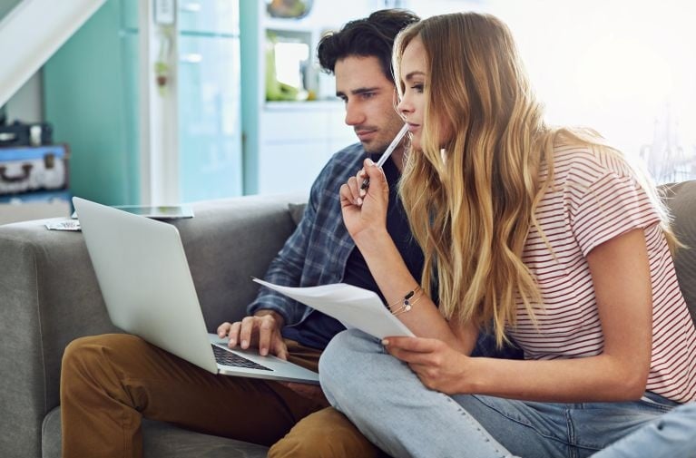 A young couple reviewing documents on a laptop at home, representing credit checks as part of the home loan application process.