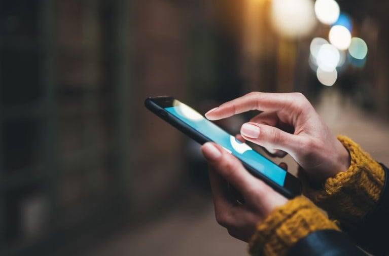 Close-up of a woman's hands using a mobile phone, representing access to QBE LMI online tools, forms, and digital resources.