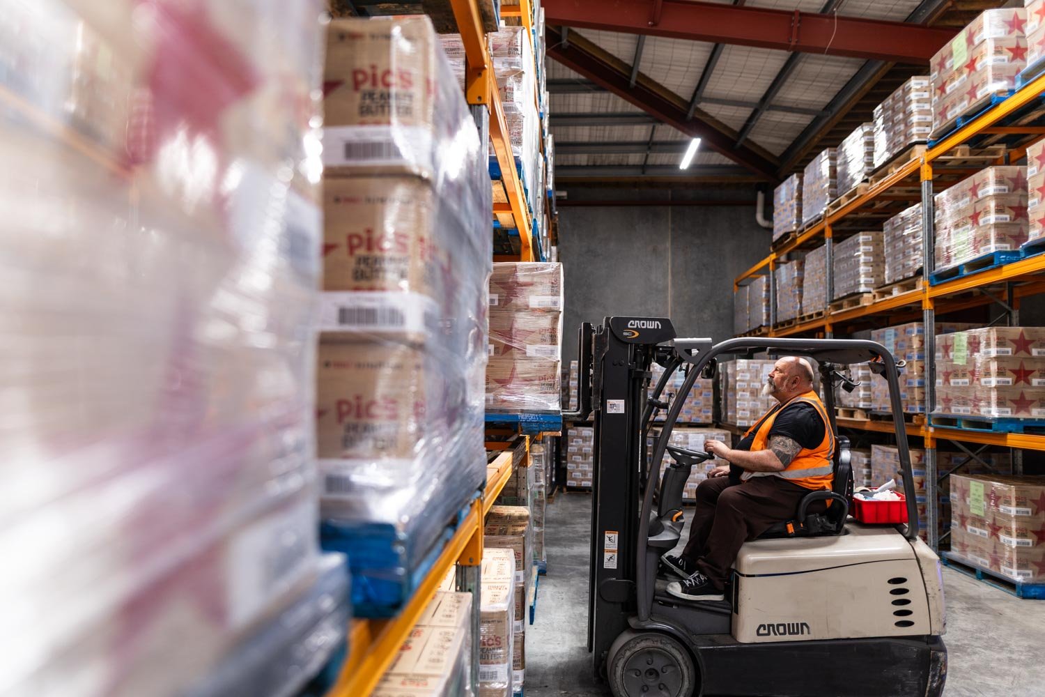 Warehouse worker operating a forklift to move palletised goods in a storage facility.