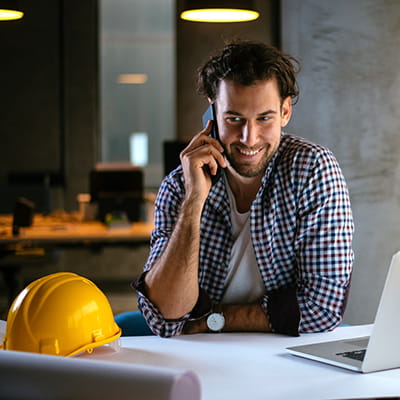 Male worker on phone with hard hat on desk