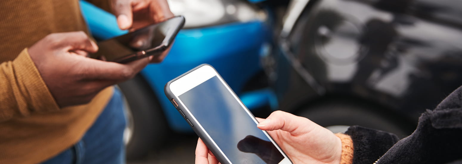 Close up of hands on phones in front of motor vehicle accident