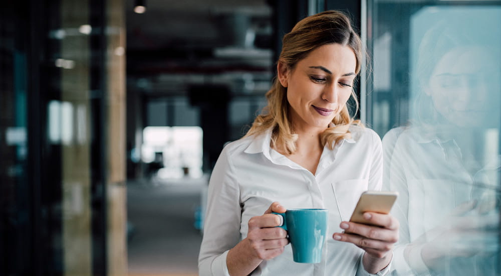 Business woman looking at mobile phone and holding mug