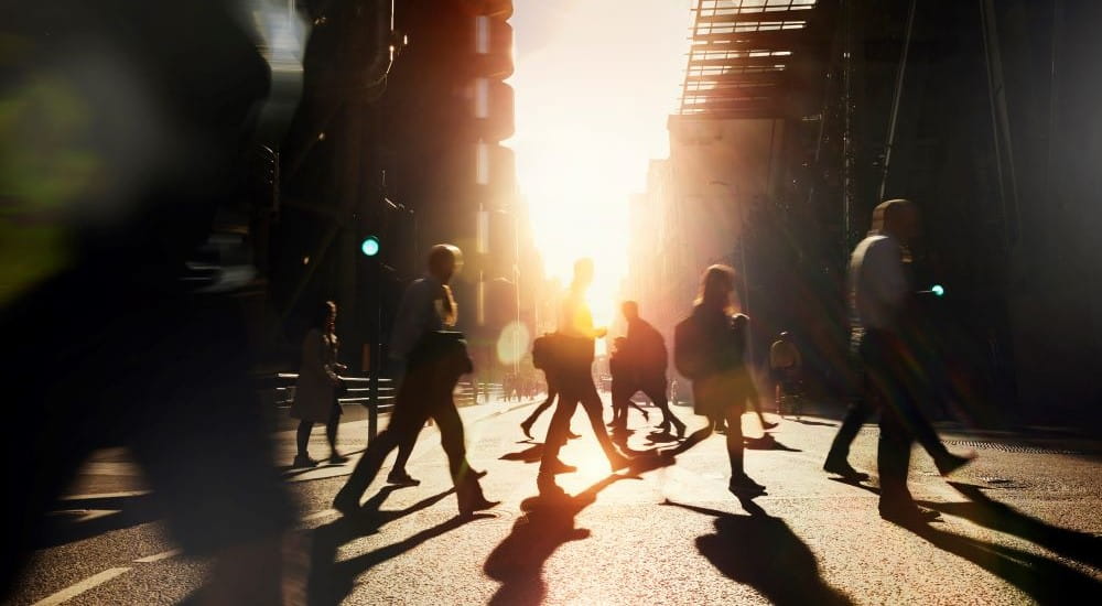 Silhouettes of pedestrians crossing a road in a city street at sunset